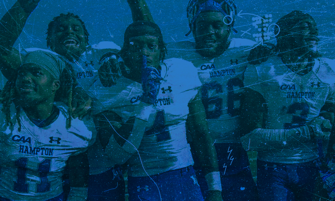 Hampton University football players in white CAA Hampton uniforms standing together with arms around each other, smiling and celebrating on the field.