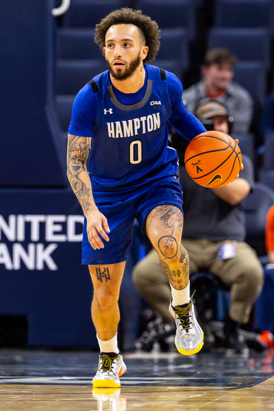 Basketball player in a blue Hampton jersey dribbling a ball on a court.