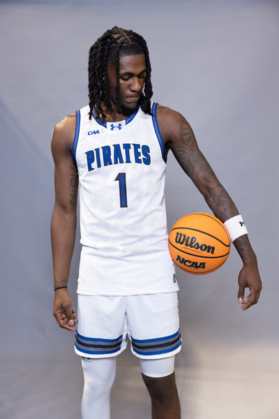 Person wearing a basketball uniform with 'Pirates' and holding a basketball on a gray background