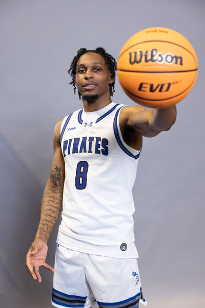 Person wearing a Pirates basketball uniform holding a basketball against a gray background