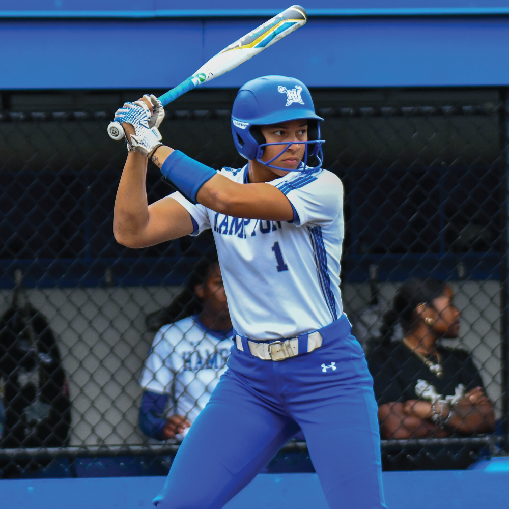 Hampton University baseball player in blue and white uniform with helmet and bat, ready to swing.