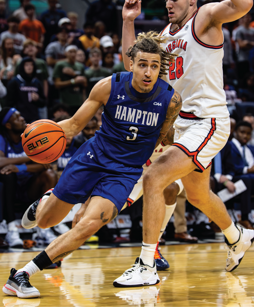Cropped image of a basketball player in a blue jersey dribbling a ball with a player in a white jersey defending during a game.