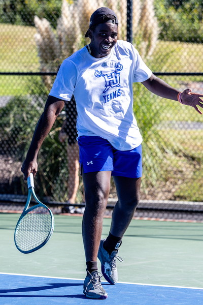 Hampton University men’s tennis player wearing a white shirt with a HU logo and blue shorts, holding a tennis racket.