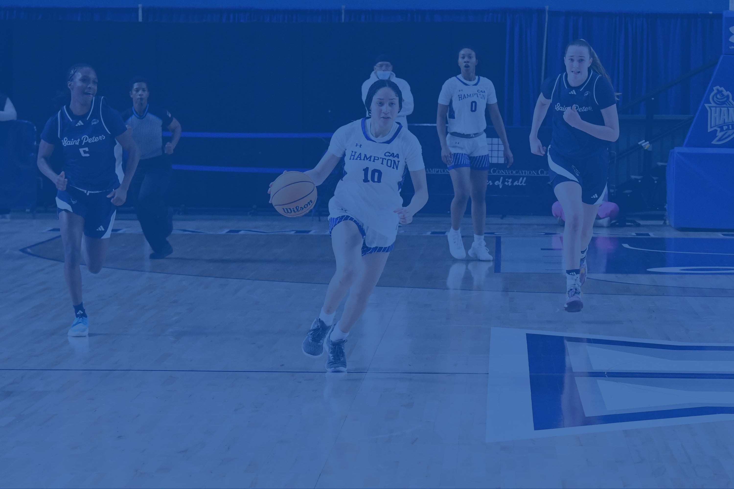 Woman playing basketball on a court with other players in the background.