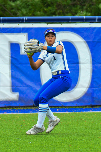 Hampton University softball player in white and blue uniform fielding a ground ball on the infield during a game.