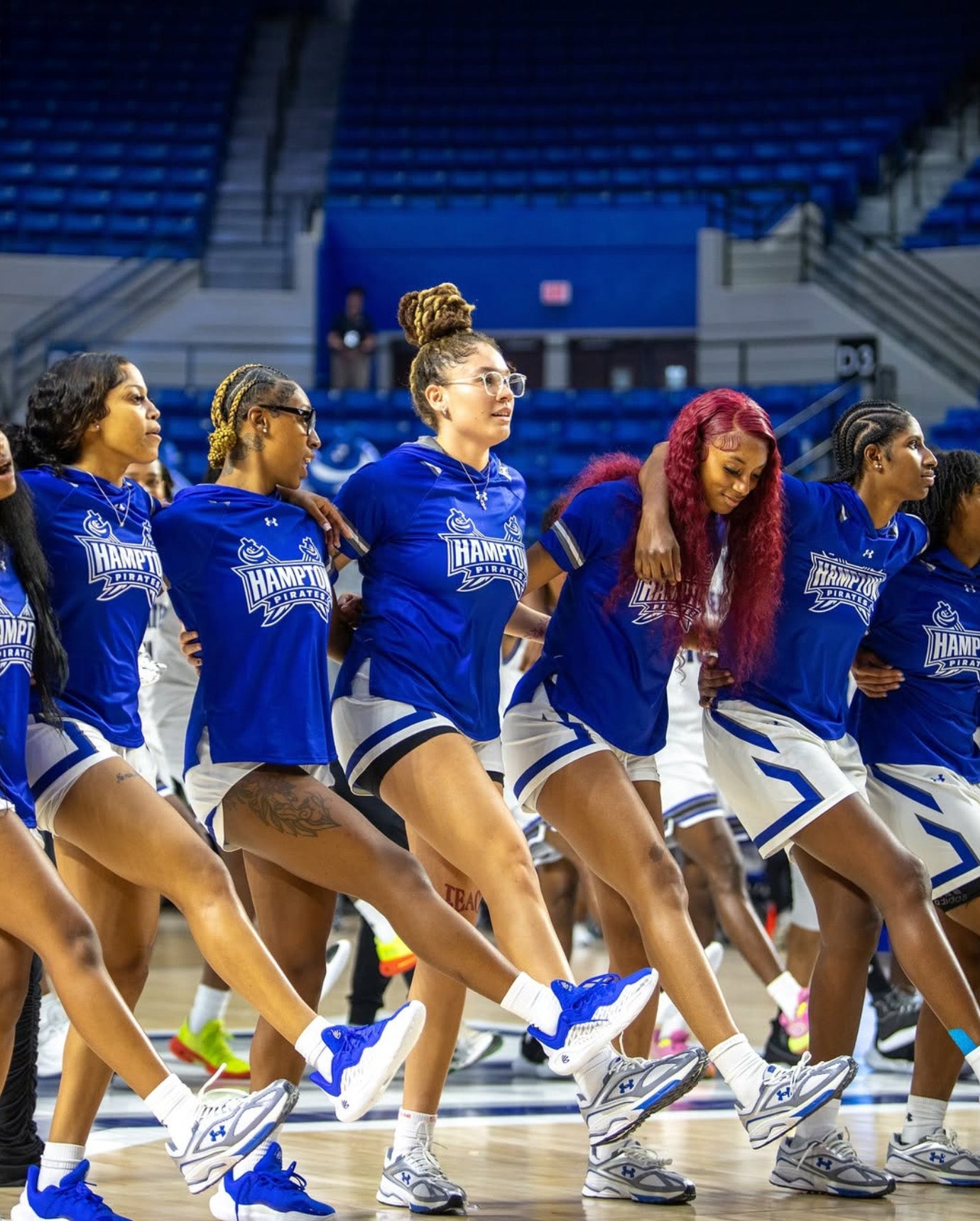 Hampton University players standing arm in arm on the court during pregame warmups at an arena.
