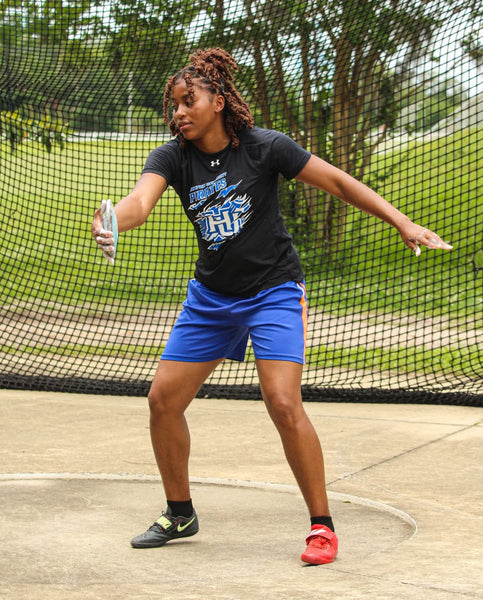 Person in athletic wear preparing to throw a discus in an outdoor setting with a netted area.